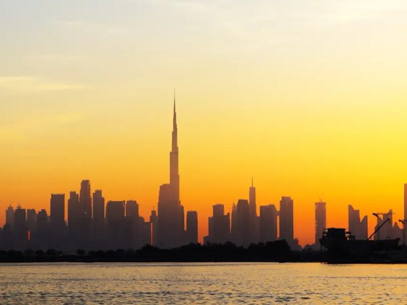Dubai skyline at sunset seen from the water, with the Burj Khalifa on the horizon